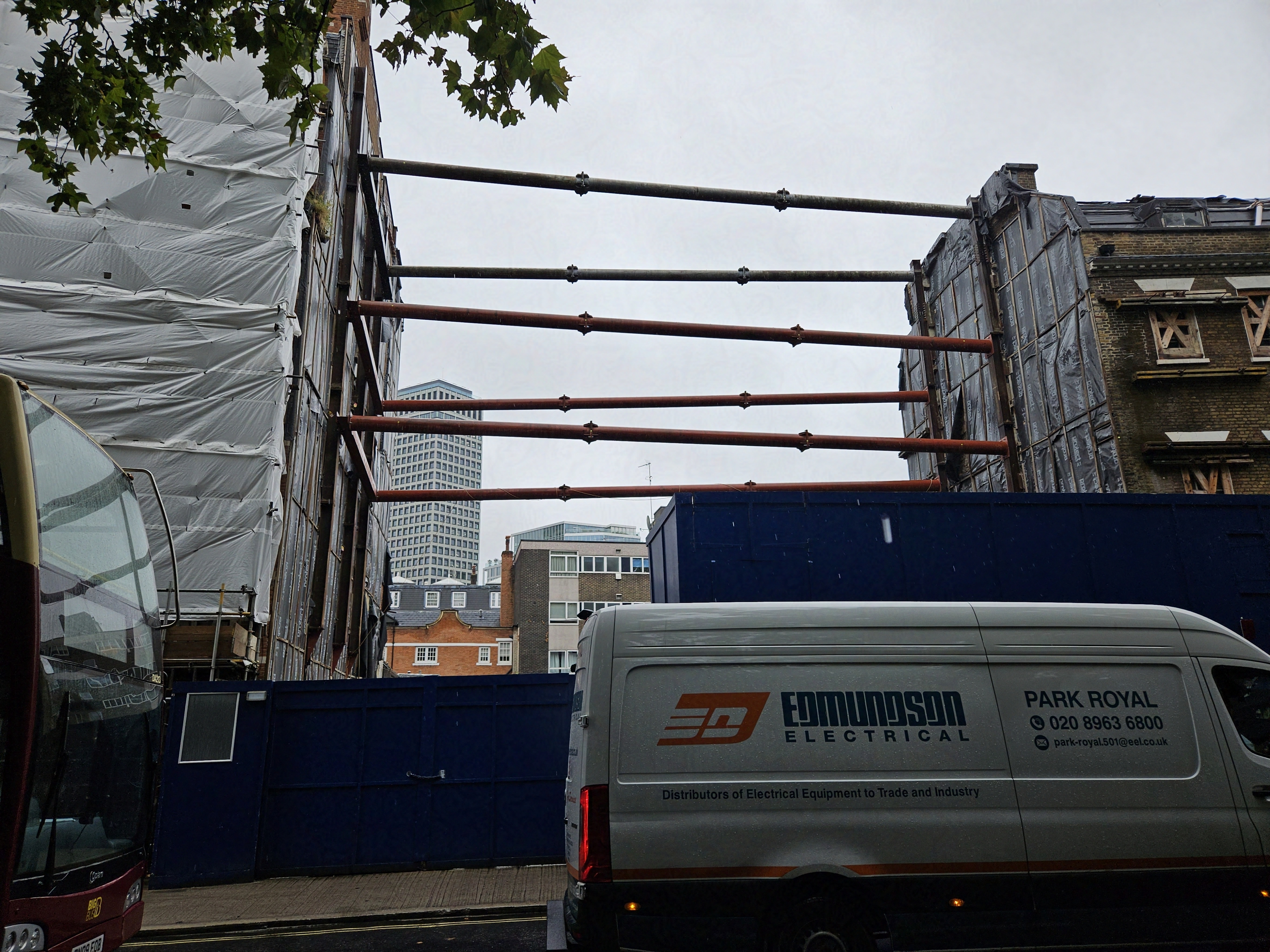Picure of a row of buildings with a middle building missing. The two adjacent buildings are held apart by giant metal pillars