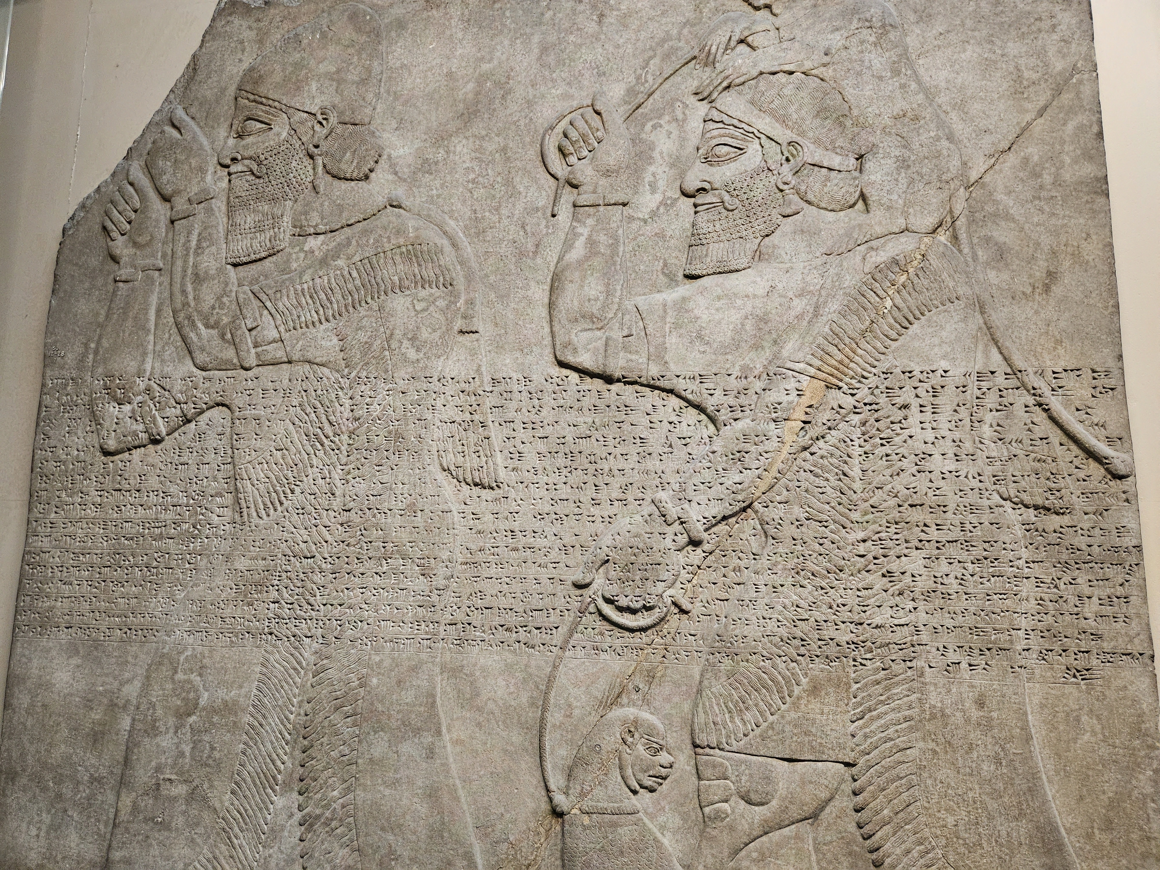 Picture of a Babylonian stele with ancient Cuneiform writings engraved through the middle of the carved illustration
